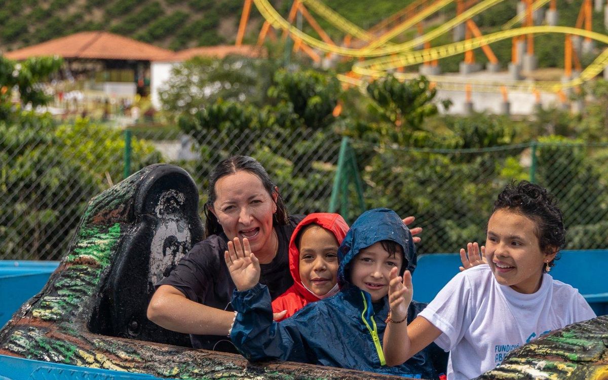 Una mamá y tres niños saludan felices desde una atracción del Parque del Café, con los cafetales al fondo